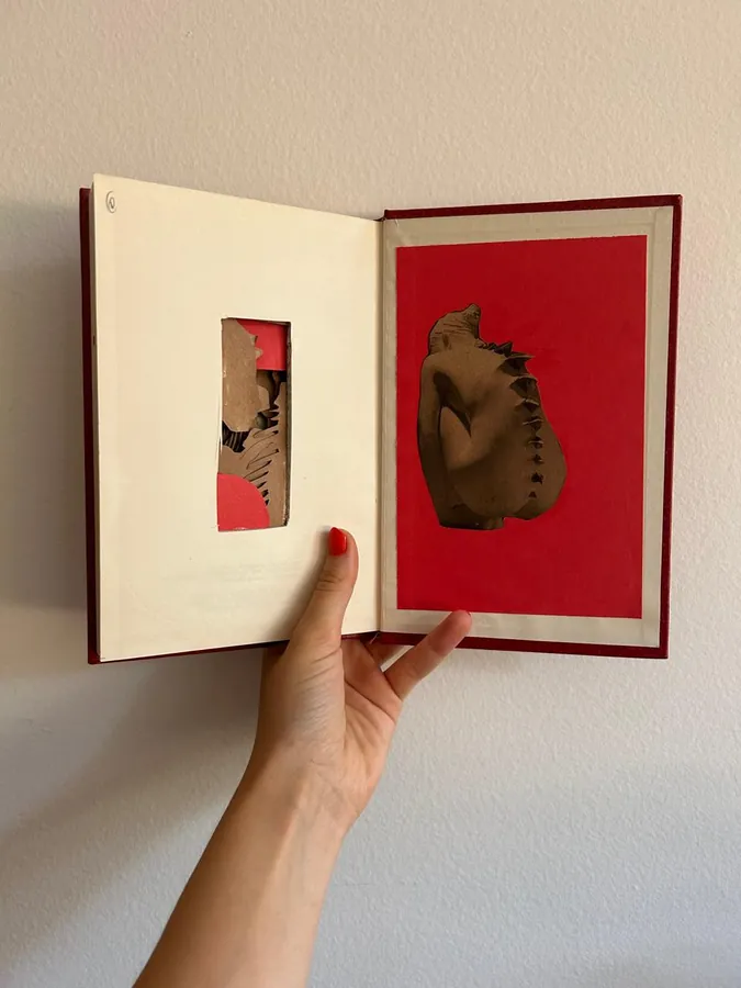 Mãos segurando um livro de artista aberto, com recorte vazado sobre fundo vermelho.