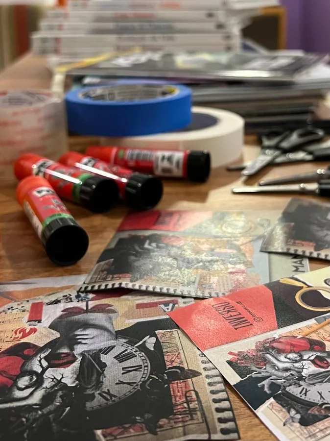 Mesa de trabalho com colas em bastão, tesouras, fitas e recortes de revista.